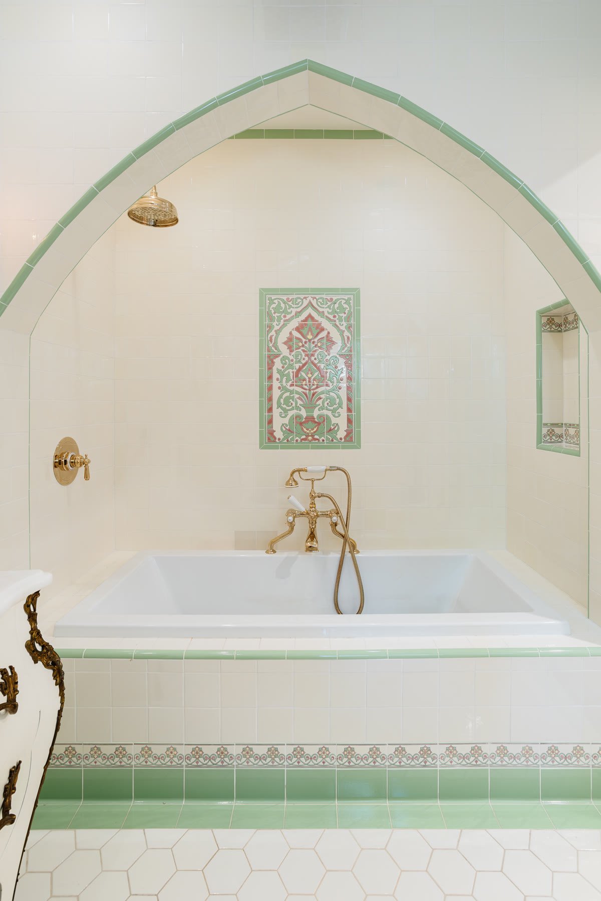 Pointed-arch tub surround in cream and green tile with a floral mural panel