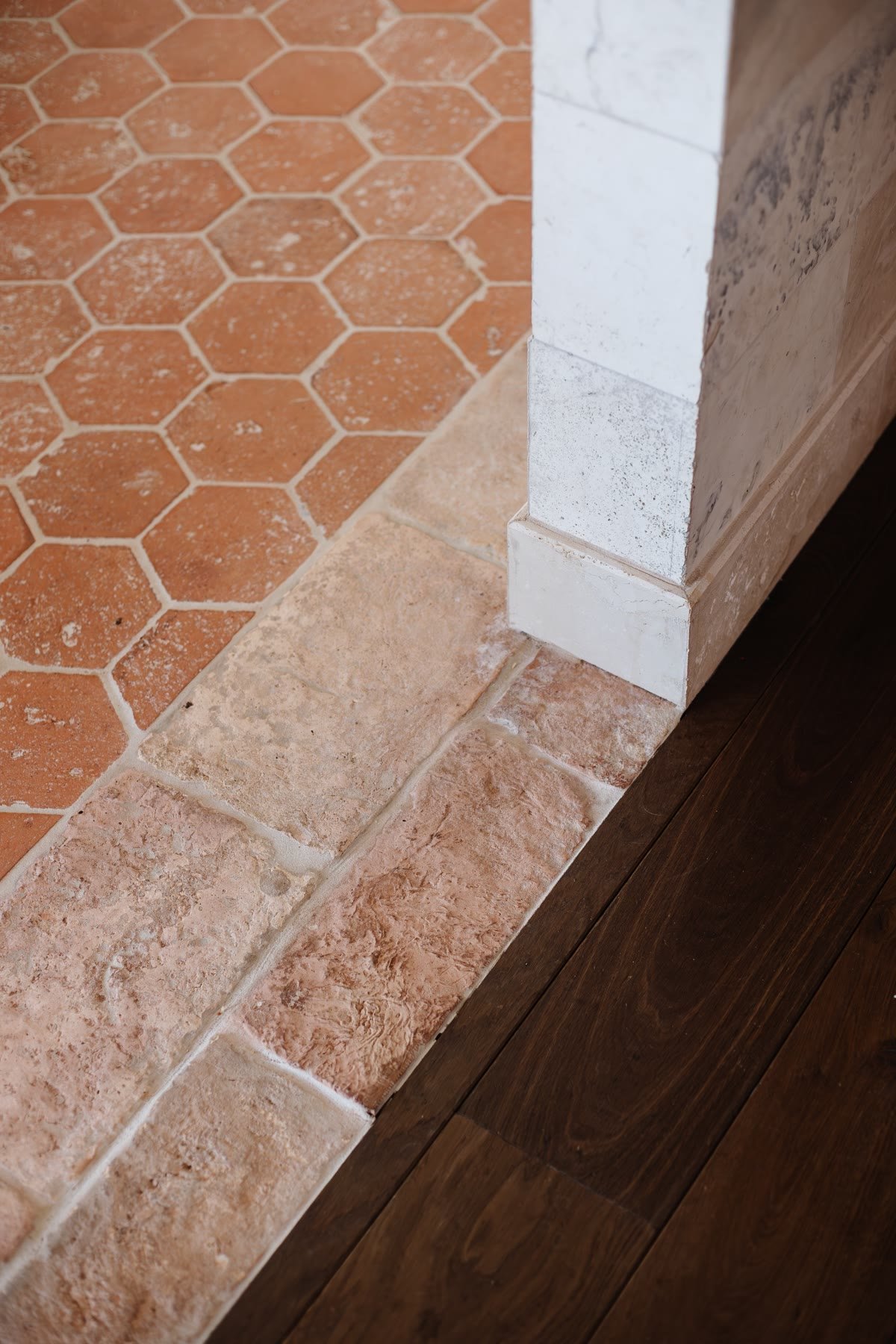Terracotta hex tile meeting a stone border and oak flooring at a marble column