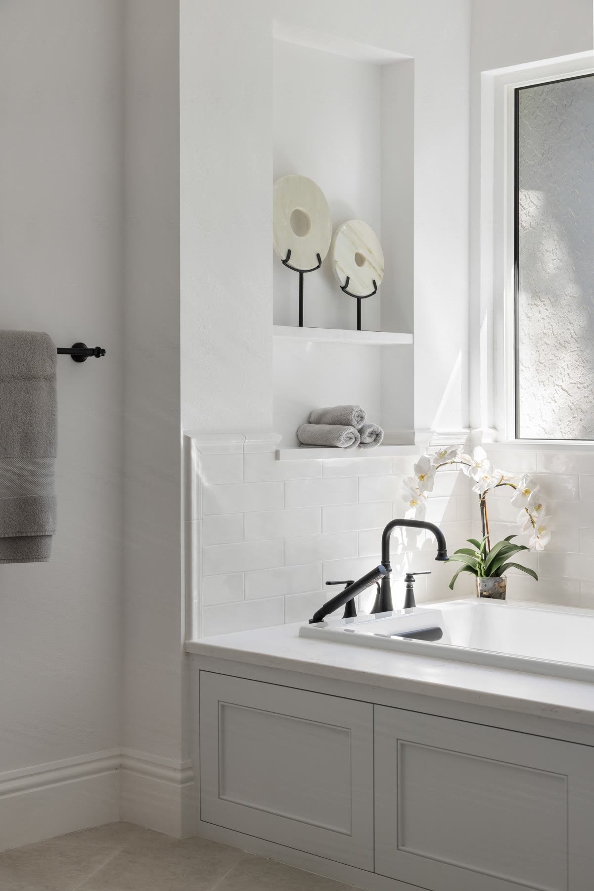 Soaking tub deck with subway tile, a window niche, and black fixtures