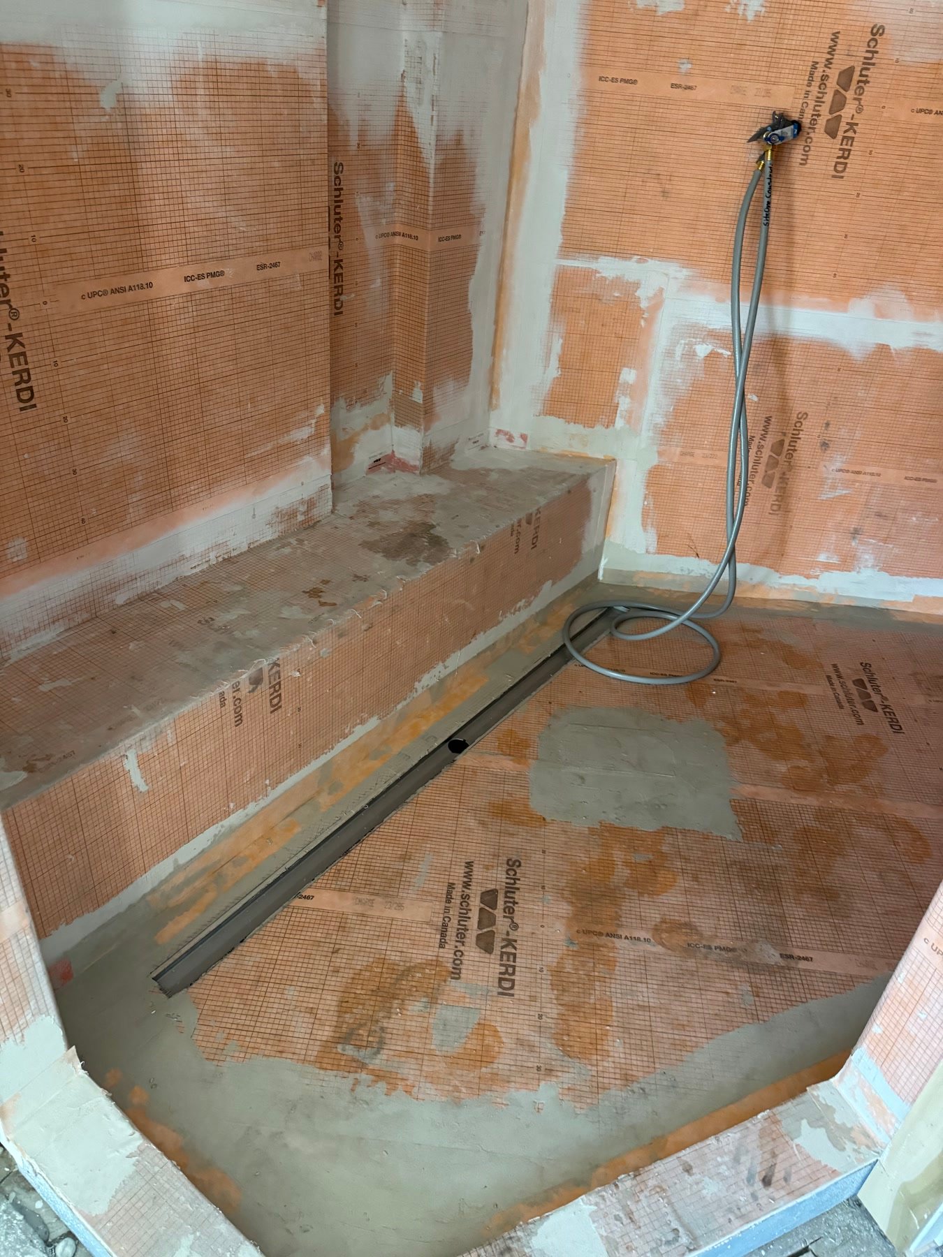 During: Kerdi-lined shower with a linear drain and a built-in bench — the shower that replaced two toilet rooms