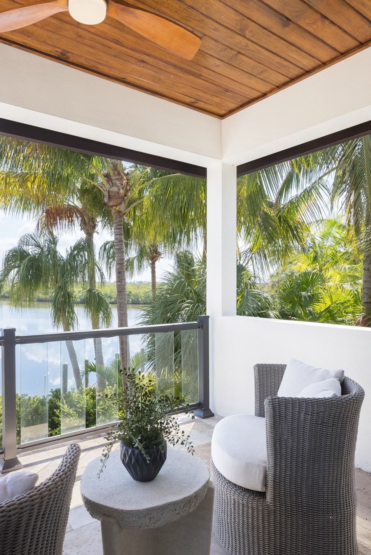 Covered lanai with a wood ceiling, glass railing, palms, and a water view