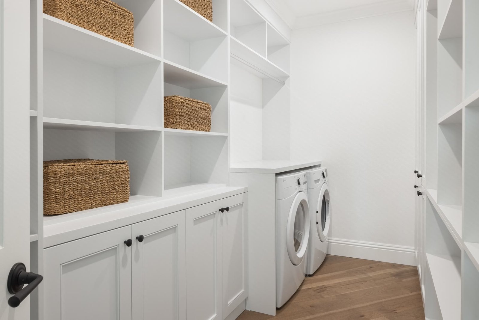 Expanded laundry and storage millwork with open cubbies, baskets, and a washer-dryer pair