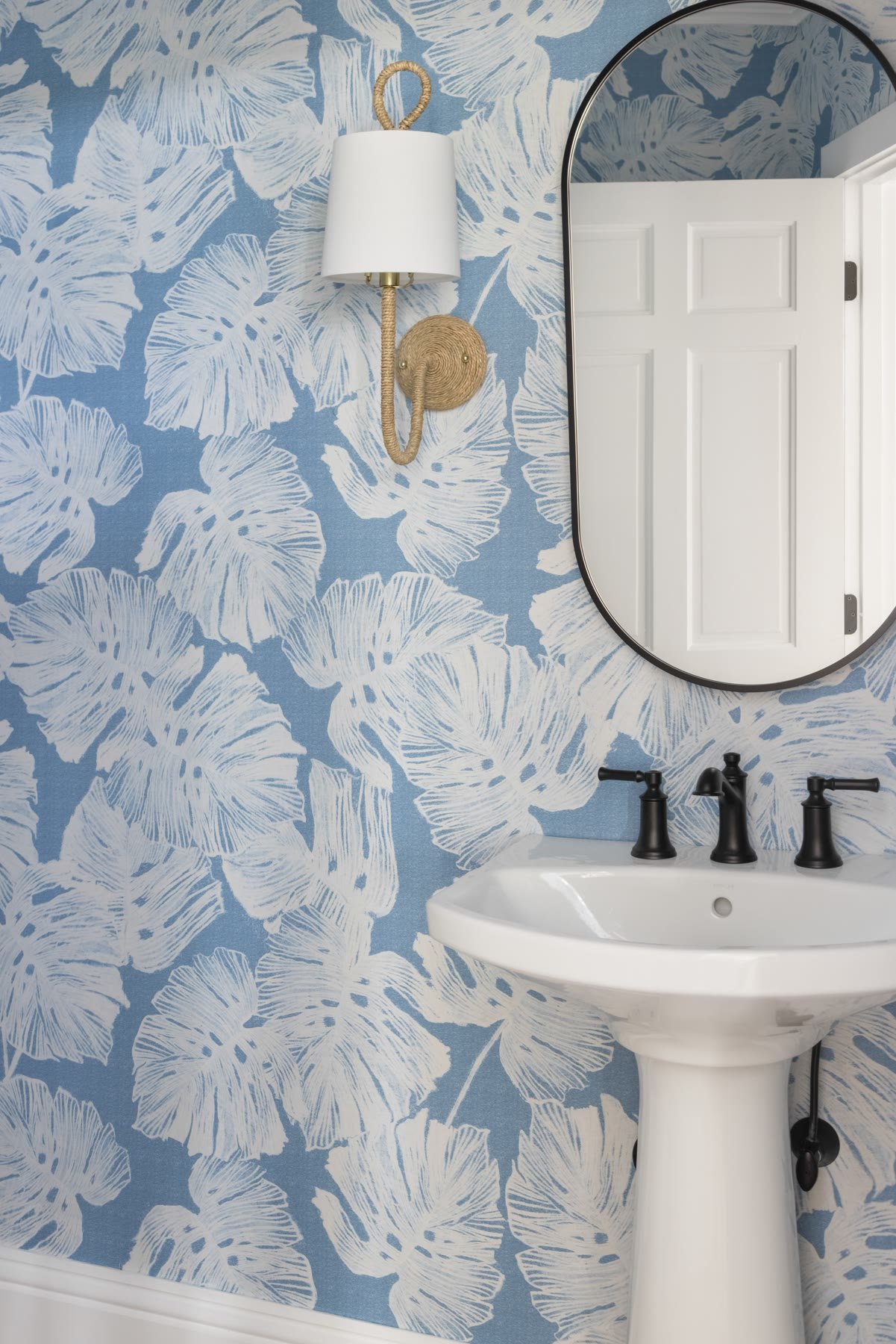 Powder room with blue leaf wallpaper, a rope sconce, and a pedestal sink