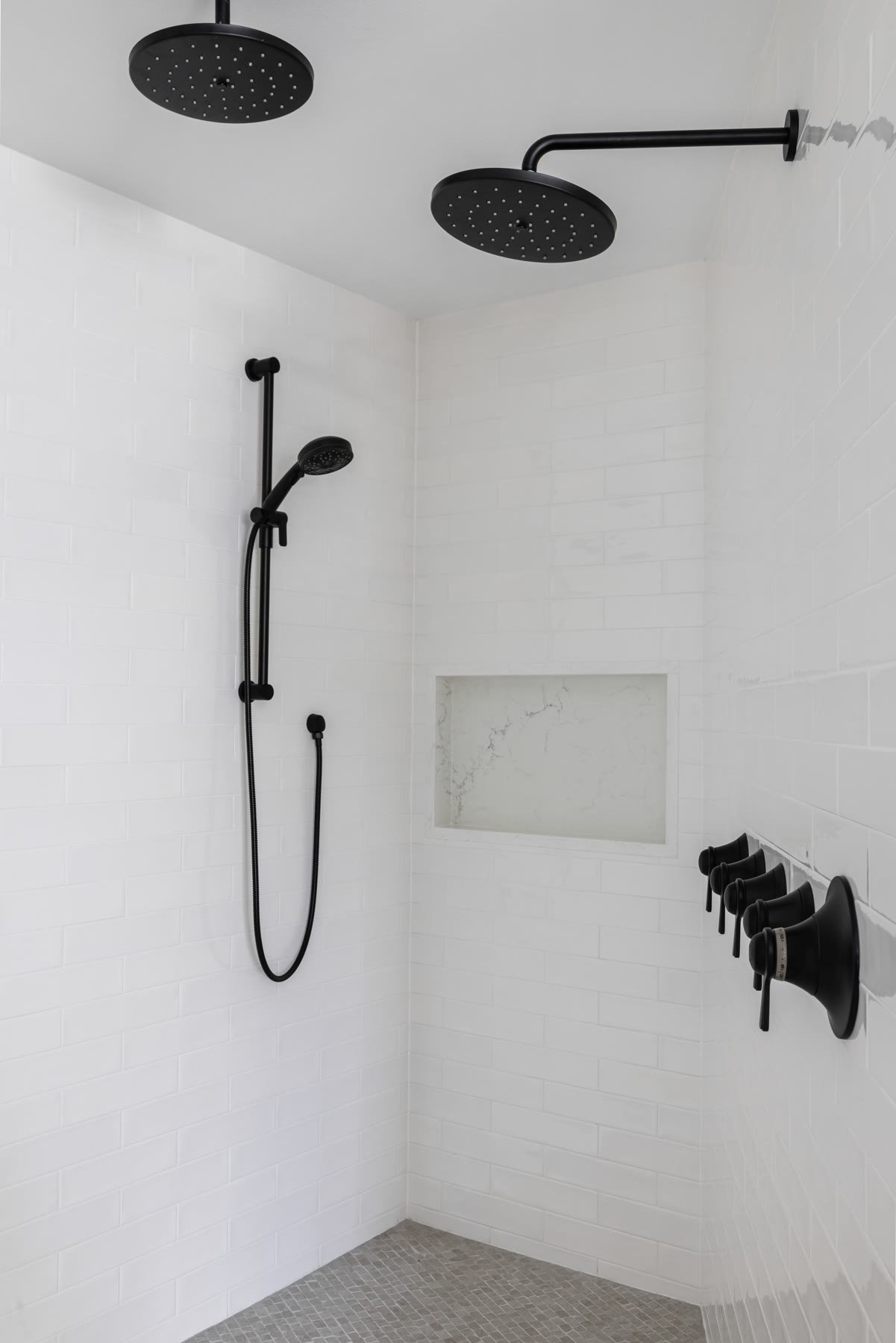 Enlarged primary shower with dual black rain heads, white subway tile, and a marble niche