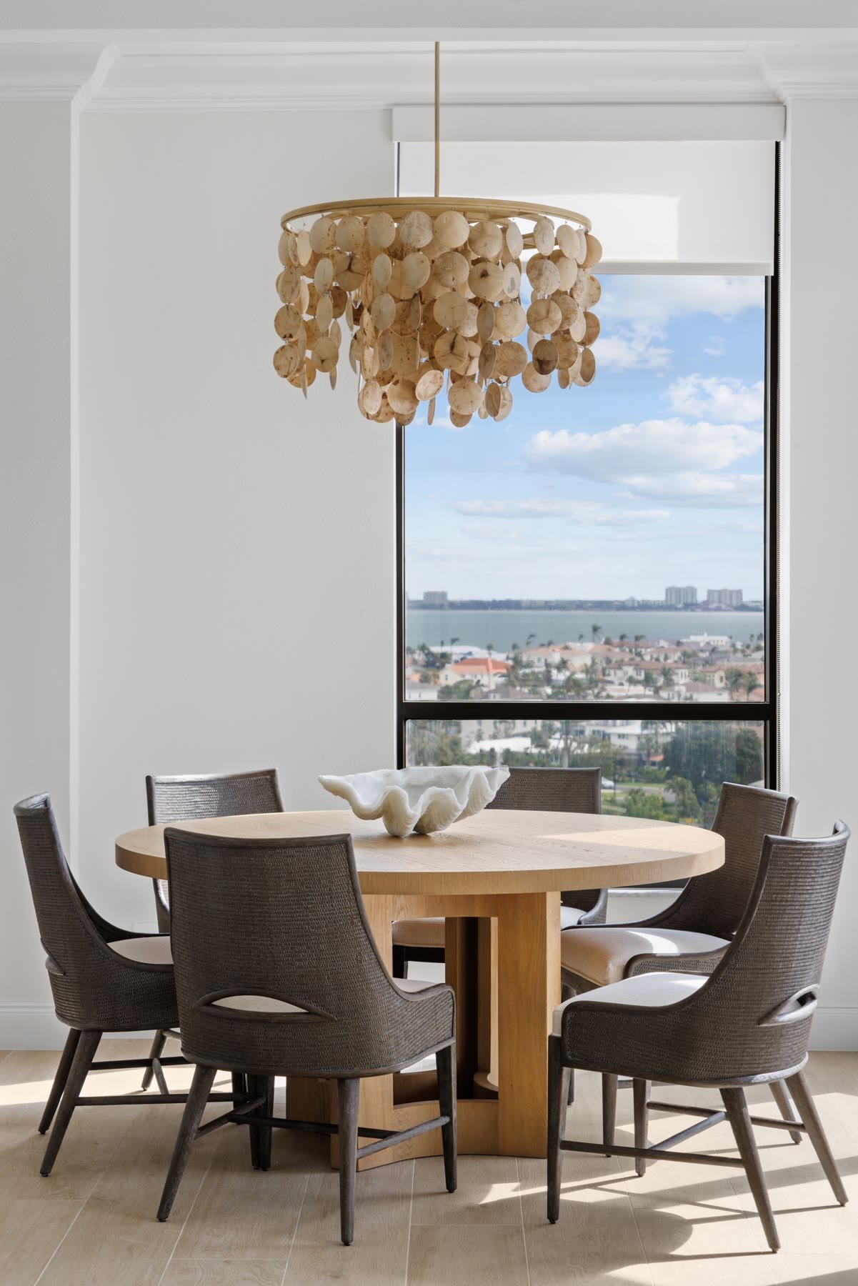 Round dining table under a capiz chandelier with Sarasota Bay beyond the glass