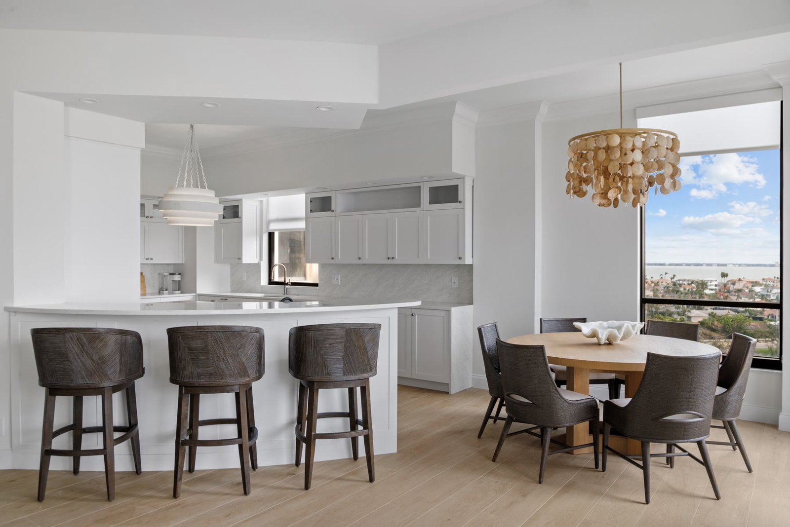 Reconfigured kitchen and dining as one room — a white island, dark stools, and a capiz chandelier against the bay view