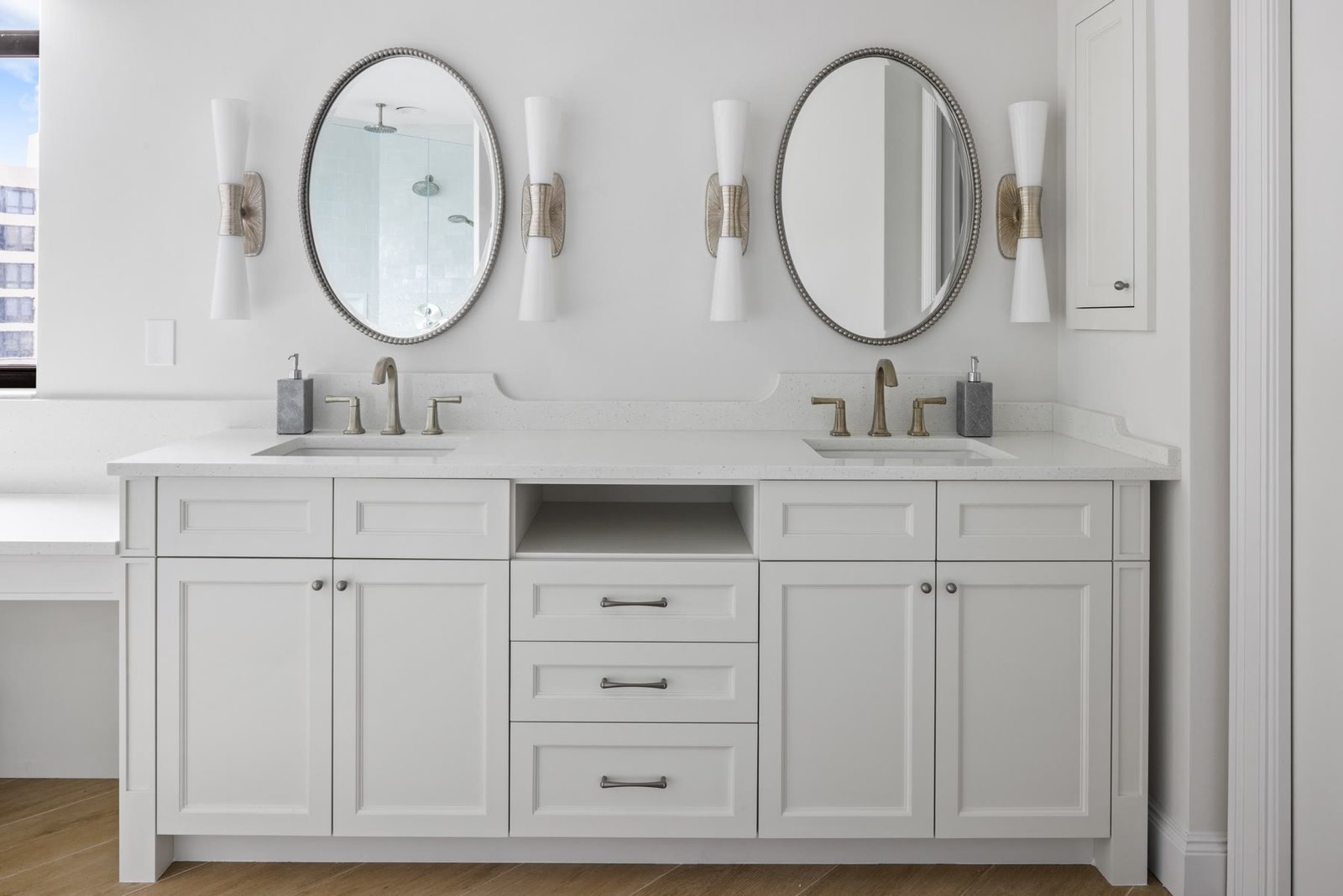 Double vanity with oval mirrors, white millwork, and a quartz counter